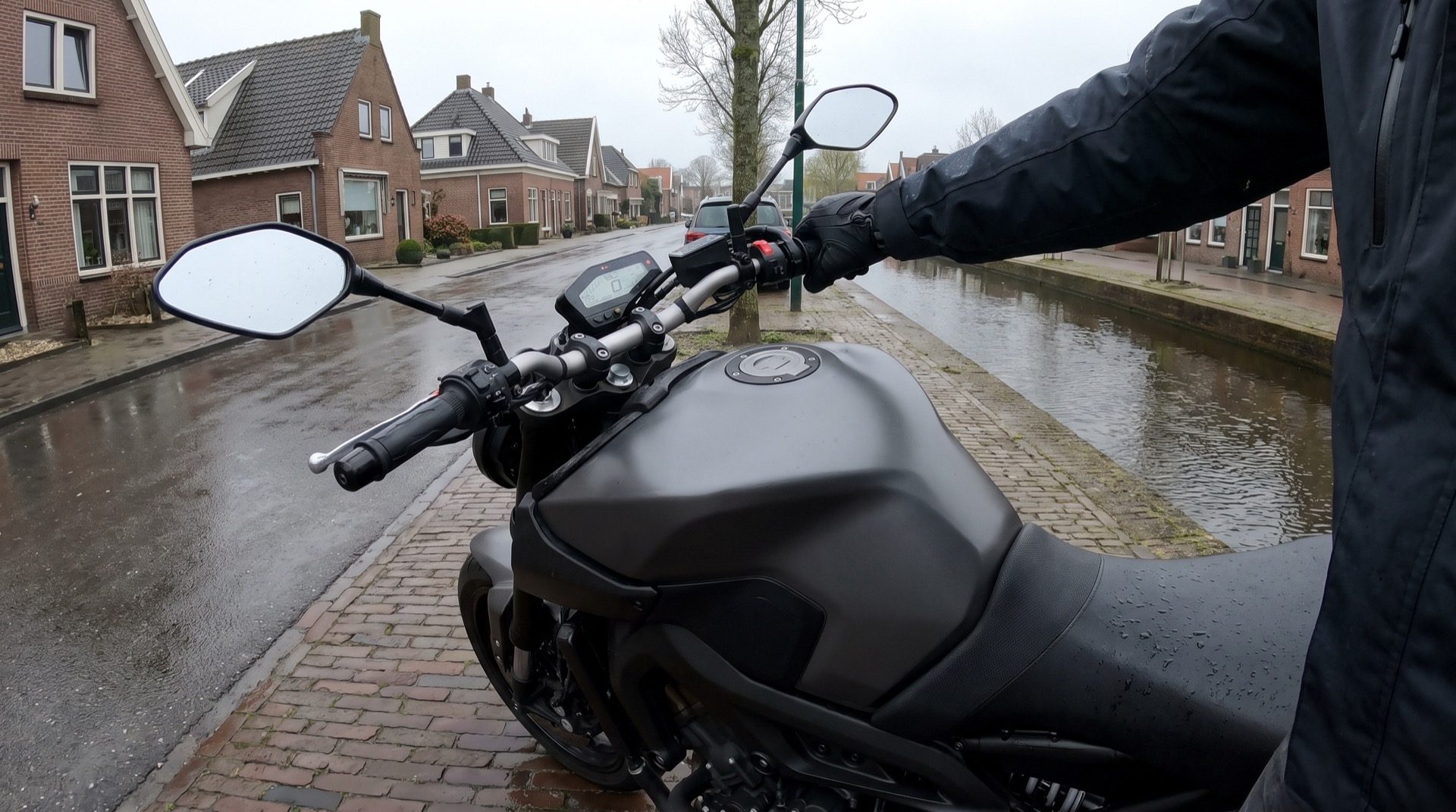 Motorrijder met handschoen aan het stuur van een geparkeerde motor in een natte straat